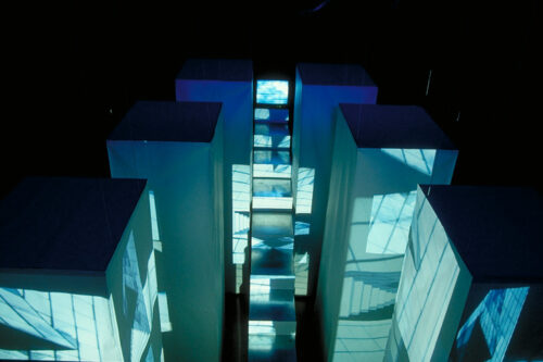 High cubes with a staircase leading up between them. On all these things are projected images of skyscraper facades